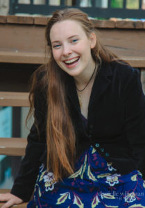 Lotus has long, lighter hair, and is smiling while sitting on a picnic table